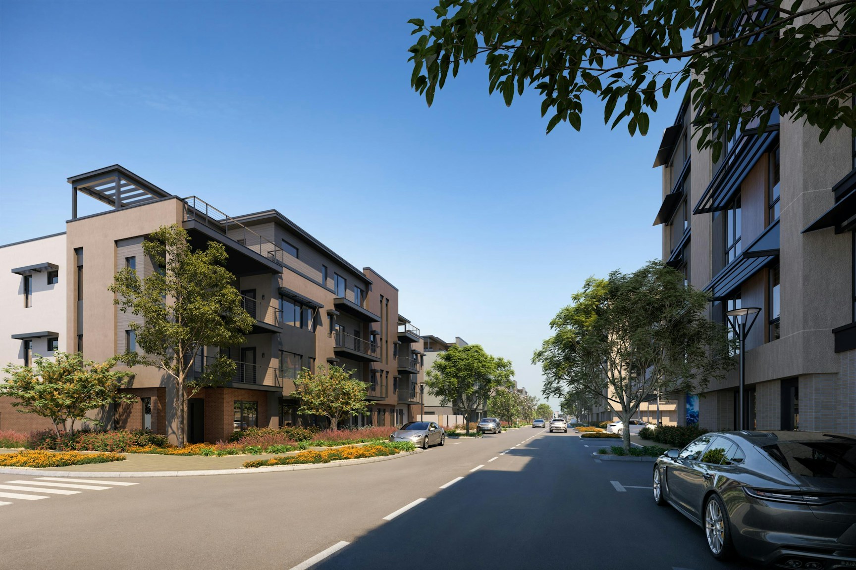A modern urban street with multi-story apartment buildings on both sides, surrounded by trees and greenery. Cars are parked along the street under a clear blue sky.